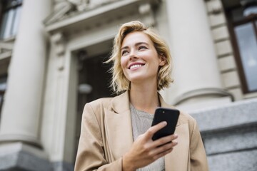 Smiling businesswoman using smartphone outdoors