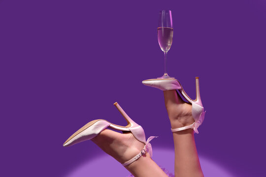 Legs of woman in high heels with glass of champagne after party on violet background