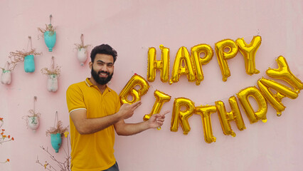 Happy Birthday Celebration with Smiling Man Holding Golden Balloons and Party Decorations Indoors