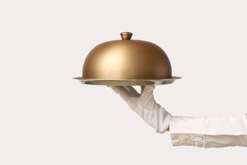Hand of waitress with metal tray and cloche on grey background