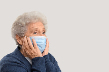 Shocked elderly woman in medical mask on grey background