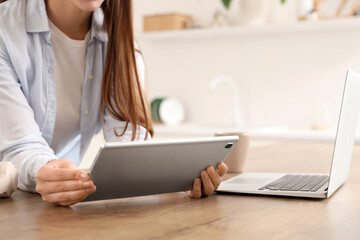 Young woman with modern tablet computer and laptop in kitchen, closeup