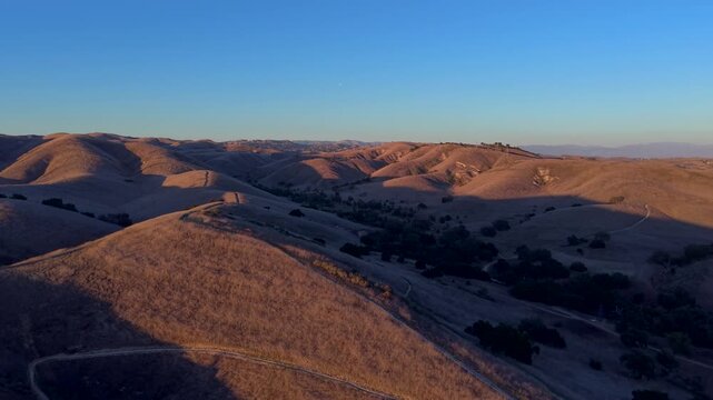 Wide drone view of Chesebro Trail in Agoura Hills, California, showing expansive rolling hills and winding trails across the Santa Monica Mountains landscape during calm golden hour subset.