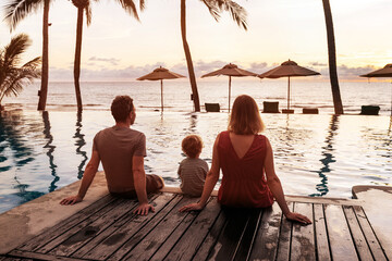 family travel to tropical sea beach, couple with child sitting near swimming pool at sunset in hotel, family vacation travel