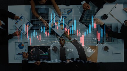 A diverse financial team collaborates in a modern office environment, analyzing digital stock market data on laptops and documents, driving business strategies forward. Raster