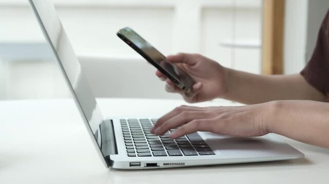 Close up man hands using smartphone and laptop computer for two factor authentication or multitasking. Business person working at office desk. Concept of digital technology, connection and finance