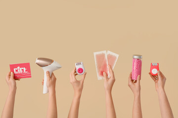 Many female hands with photoepilator, wax strips, epilators and gift card on beige background. Depilation concept