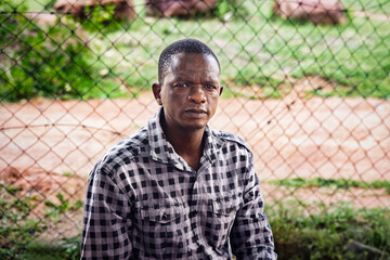 Isolated african man stands before chain-link fence barrier. Themes of human rights, freedom, restraint, and being a dissident