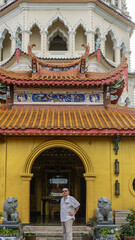 A man stands at the entrance to the Chinese pagoda. There are lion sculptures nearby. A temple with tiled roofs, curved cornice edges, arches, columns. Malaysia. Penang. Georgetown. Kek Lok Si Temple. © Вера 