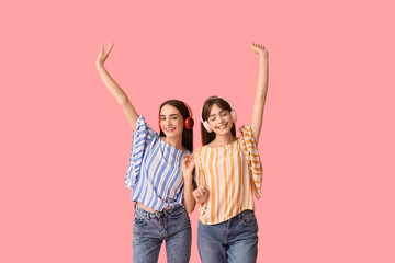 Fototapeta premium Beautiful young twin sisters in modern headphones on pink background