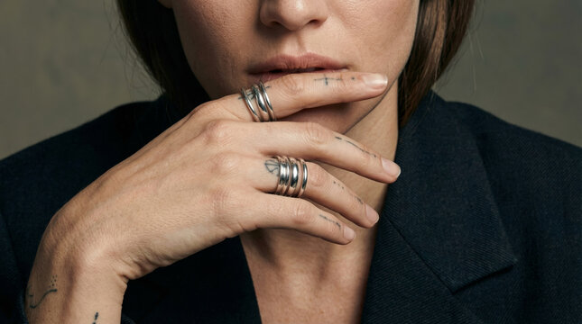 Woman wearing stacked silver rings and minimalist fine line finger tattoos covering mouth