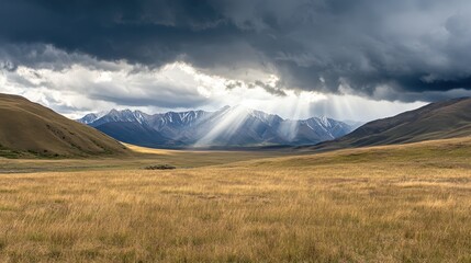 Sunbeams break through dark storm clouds over a vast mountain range and golden field