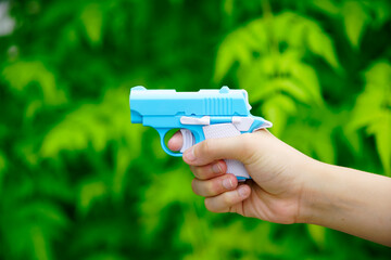 Hand Holding Bright Blue Toy Handgun Against Green Foliage Background