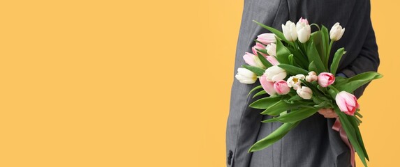 Young man with bouquet of beautiful tulips on yellow background with space for text, closeup