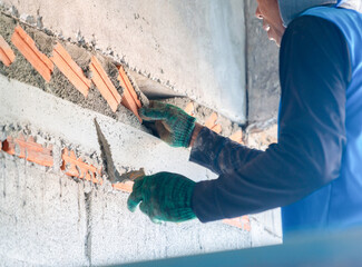A construction worker using a trowel to apply mortar while laying red bricks