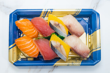 A takeaway box with assorted nigiri sushi pieces including salmon, tuna, and mackerel.