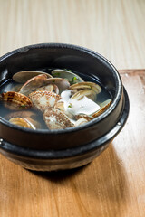 A black bowl filled with clam soup featuring fresh clams and tofu in clear broth.