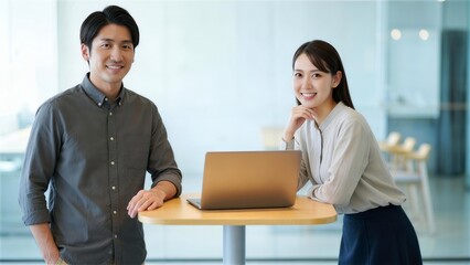 ハイテーブルでパソコンを開き明るく微笑む男女の社員