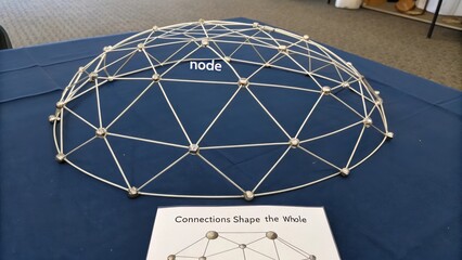 Geometric geodesic dome structure model displaying interconnected nodes and connections, set on a table with explanatory materials.
