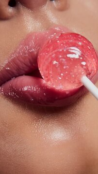 Ultra close-up macro of glossy pink lips and sparkling translucent lollipop in mouth with detailed skin texture and juicy candy shine
