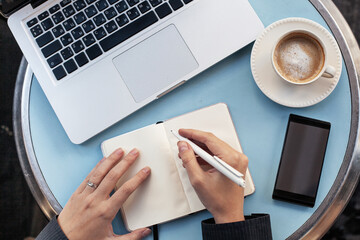 new year resolutions writing, intentions, female hands with paper notepad, pen, smartphone and laptop computer