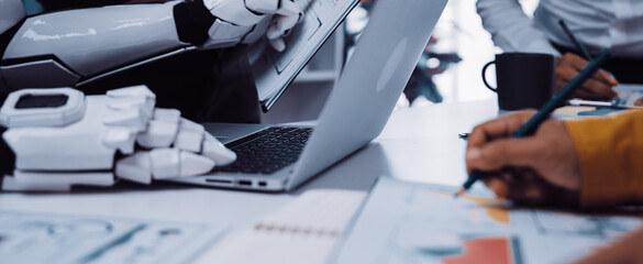 A dynamic office scene showing a robot collaborating with humans, featuring a laptop and charts, illustrating the integration of technology in modern business practices.Noogenesis