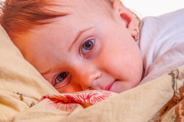 Close up portrait of baby awake under blanket at bedtime.