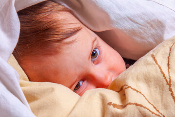 Close up portrait of baby awake under blanket at bedtime.