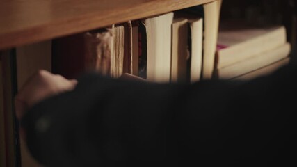 Hand placing book on shelf in cozy library setting, warm and nostalgic feel