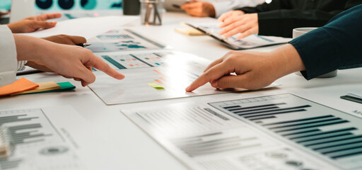 A diverse group of professionals collaborates in a modern office, analyzing business charts and graphs during a meeting. The scene highlights teamwork and communication. SACTR