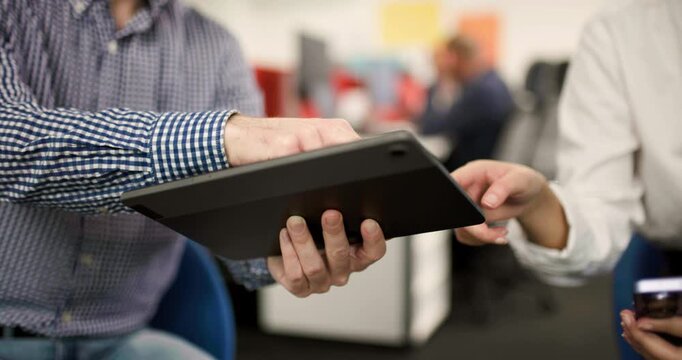 Team members collaborate on a project in an office setting using a tablet to share ideas and gather feedback during a busy workday
