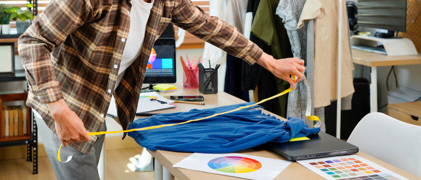 male tailor measuring shirt with tape measure at work studio