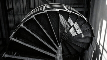 Spiral staircase interior with sunlight shining through windows, black and white photography, industrial architecture detail, closeup view