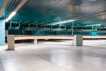 Empty abandoned wardrobe room interior at derelict Tallinn City Hall with turquoise tiled walls, numbered clothing hooks, corrugated metal ceiling, fluorescent lights, and concrete floor surface
