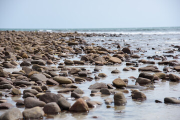 Rocks/stones on the  beach during a daylight on the islands, Thailand.Background image of the beach with sea in the distance with pebble stones.