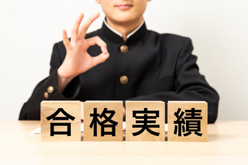 「合格実績」と書かれたブロックとOKサインをする男子学生