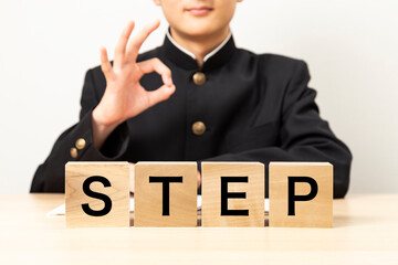 「STEP」と書かれたブロックとOKサインをする男子学生
