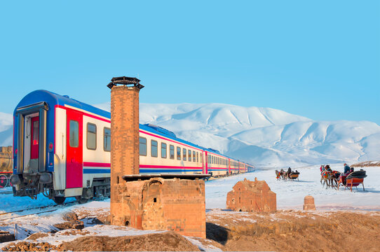 Red diesel train (East express) in motion at the snow covered railway - Horses pulling sleigh in winter - Ani Ruins, Ani is a ruined and  medieval Armenian city - Kars, Turkey