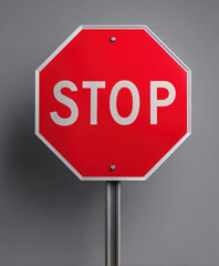Red octagonal stop sign on metal post against gray background conveying caution and traffic control