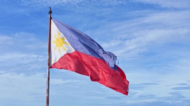 Philippine flag waving in the wind against a clear blue sky. The scene emphasizes fabric texture, natural movement, and national symbolism in outdoor conditions.