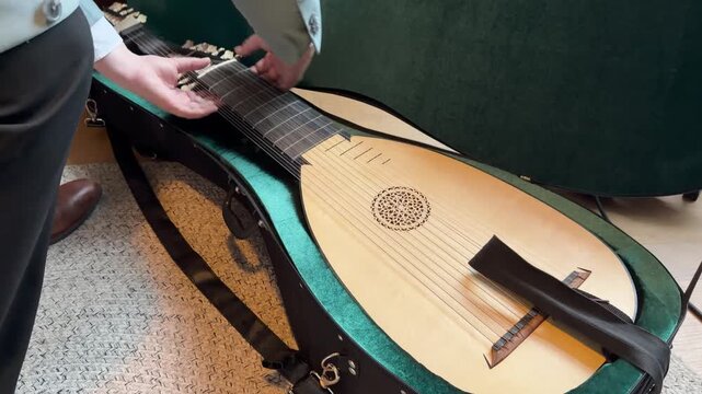 A close-up of a person opening an antique instrument case, revealing a baroque lute inside, on a cozy indoor setting.