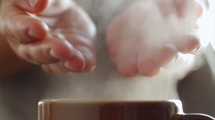 Hands outstretched over a large mug of a freshly poured hot drink, with intense steam rising and enveloping the palms, concept of warming up and sensory pleasure