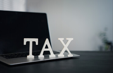 Tax concept with wooden cubes spelling TAX on office desk. Businessman calculating tax return using laptop and calculator. Financial planning and income tax preparation for business or individual use