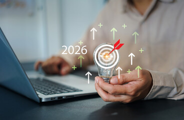 Businessman targeting future goals with lightbulb and dartboard concept, symbolizing 2026 innovation, business strategy, vision planning, and upward growth direction.