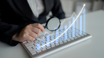 A business analysis scene showcasing a hand holding a magnifying glass over a keyboard, with virtual graphs highlighting growth trends in financial data. Impute