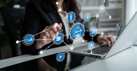 A businesswoman interacts with a laptop, utilizing a digital interface for agile project management, showcasing modern technology in a dynamic workspace setting. Tessel