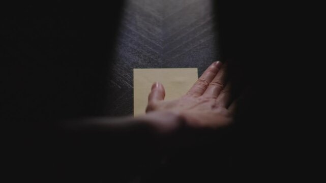 Slow motion close up footage of a hand writing out "Bonjour" on a paper note and placing it on a table. Shot in dramatic lighting for an impressive title or transition.