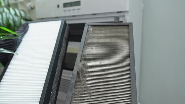 A technician wearing gloves replaces the air filter in the air purification system. The old and new air filters.