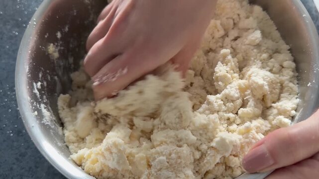Close-up of a woman's hands kneading shortcrust pastry in a bowl. The cooking process.