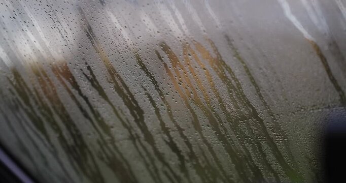 Close‑up shot of condensed water droplets streaming down the inside of a camper van window on a cold, damp day, forming vertical streaks on the glass with blurred outdoors beyond.